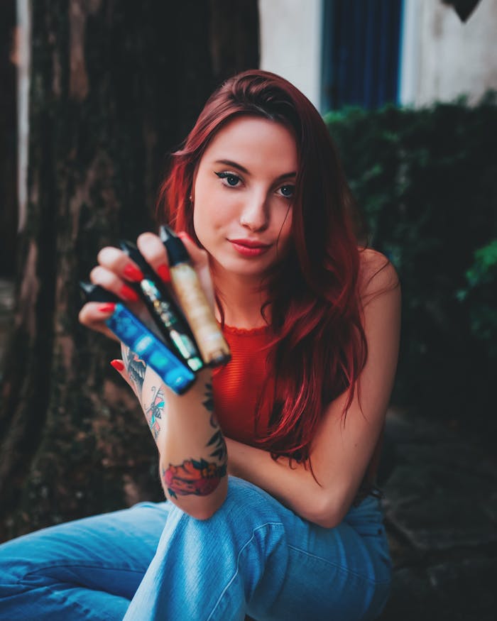 Young woman with tattoos holding multiple electronic cigarettes, showcasing colorful vapes.