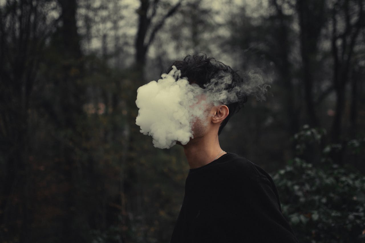 A person's face covered by smoke, creating a mysterious and artistic effect in the forest setting.